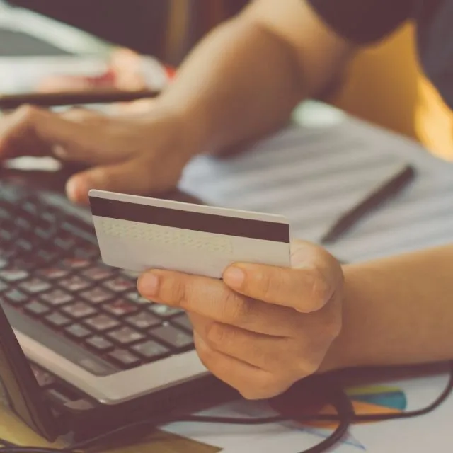 Une main tient une carte bancaire devant un ordinateur portable